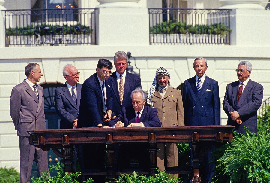 Israeli Minister of Foreign Affairs Shimon Peres signs the Oslo Accords outside the White House, alongside PLO Chairman Yasser Arafat. See Photo Credits.